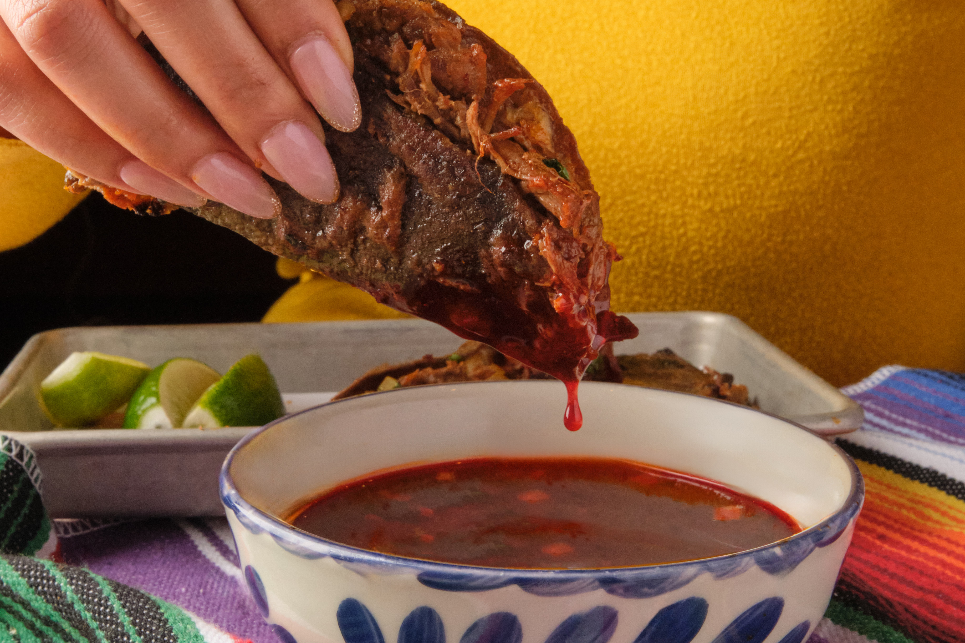 A taco being dunked into a bowl of rich consomme