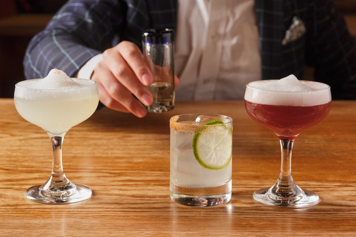 a person sitting at a wooden table with three cocktails.