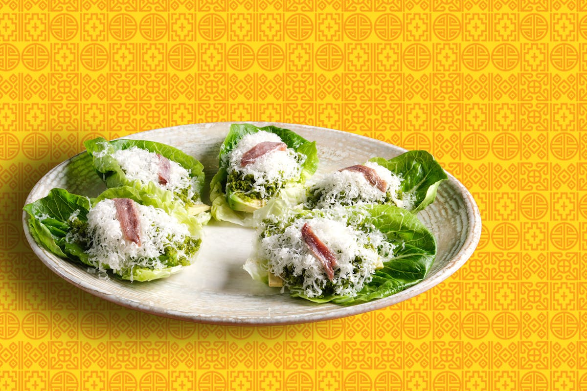 five pieces of lettuce with shredded cheese and anchovies on a white plate.