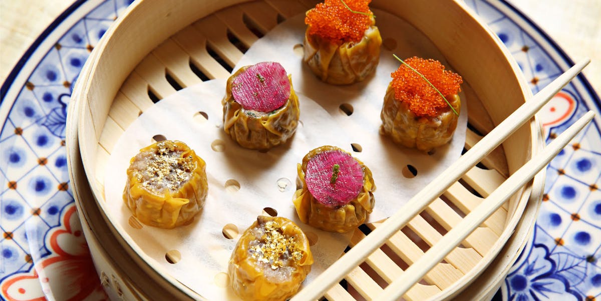 six dumplings steaming in a bamboo basket.
