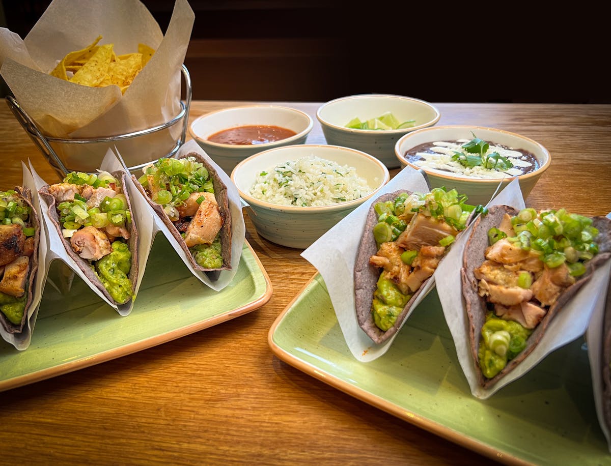 two trays of tacos with small bowls of dips and toppings.