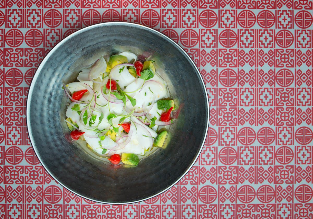 a bowl of white fish, red peppers, avocado, red onions, and microgreens.