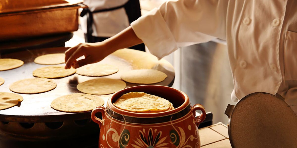 tortillas being cooked and stored in a red vessel.