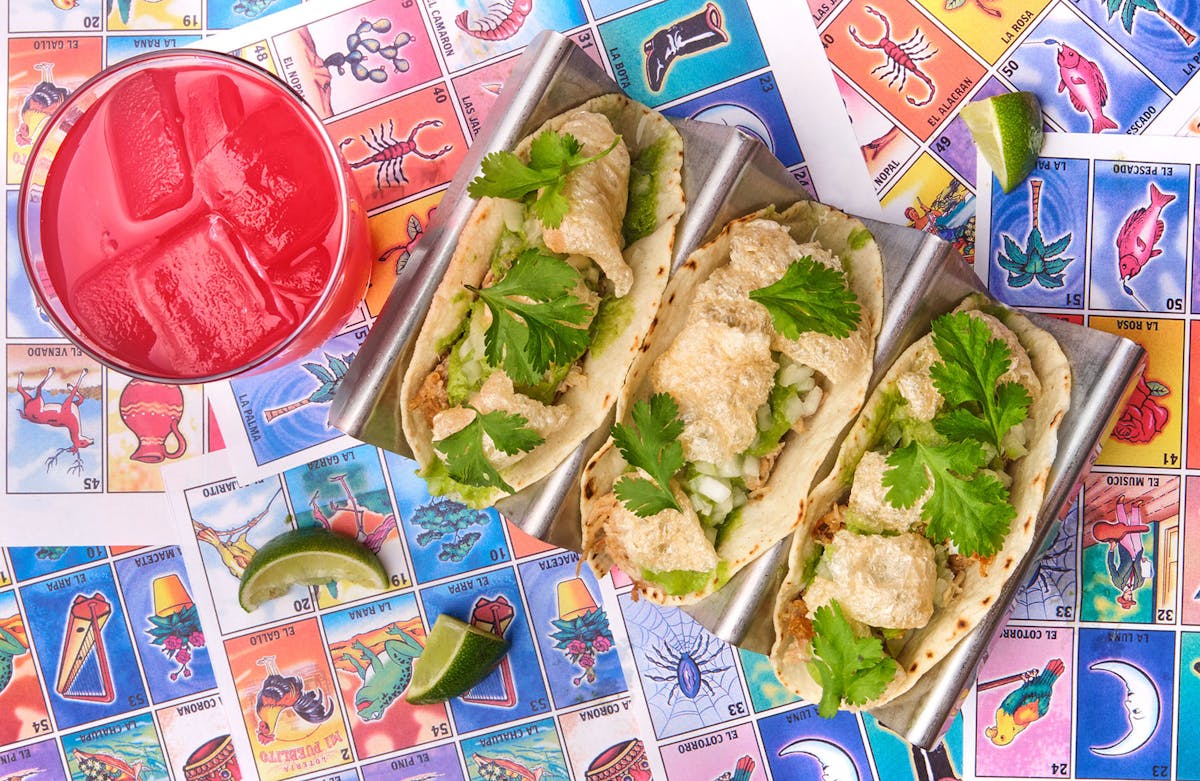 a tray of tacos next to a pink cocktail.