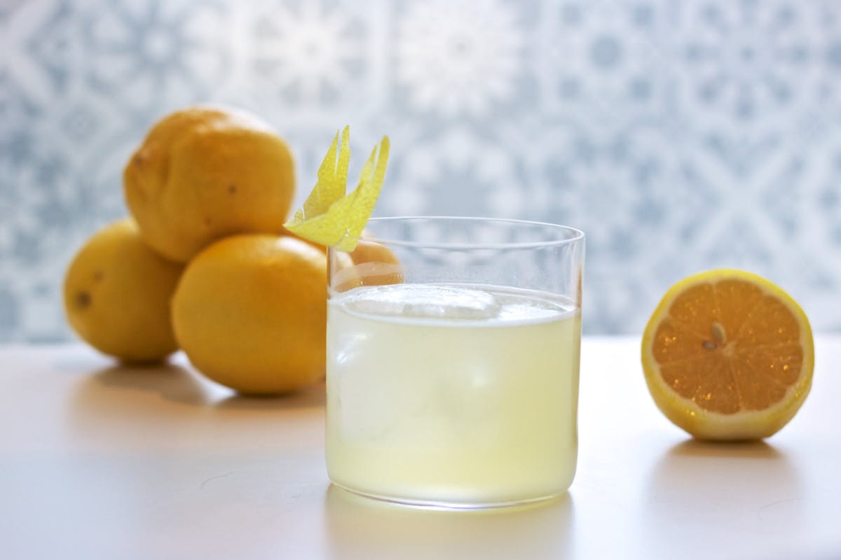 a glass of a yellow cocktail with lemons behind it.