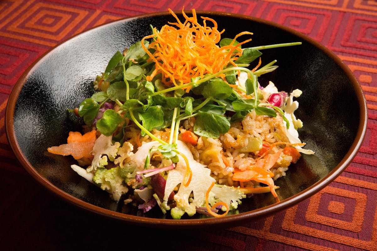 a black bowl of rice and vegetables, topped with green lettuces and shredded carrots.