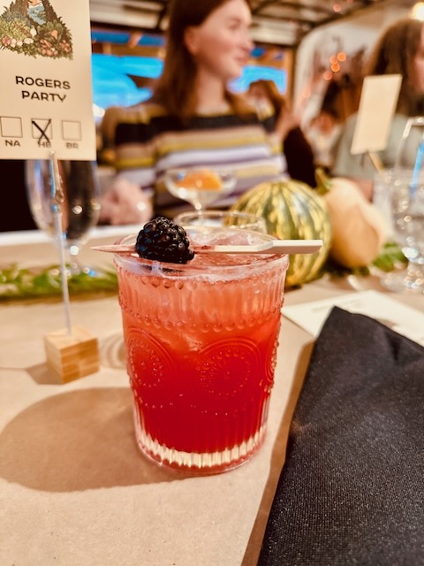 a glass of red drink with a black berry on top