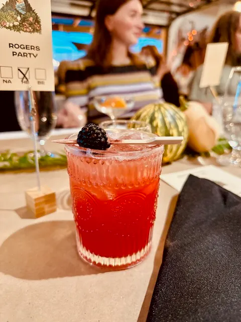 a glass of red drink with a black berry on top