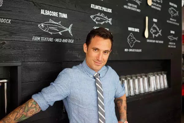 Photo of man with shirt and tie against a black wall with outlines of fish