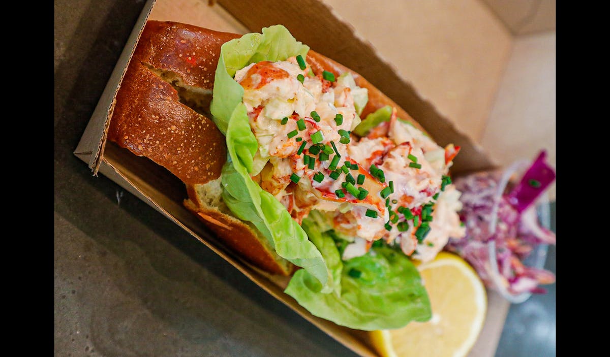 maine lobster roll with a lemon in a take out container
