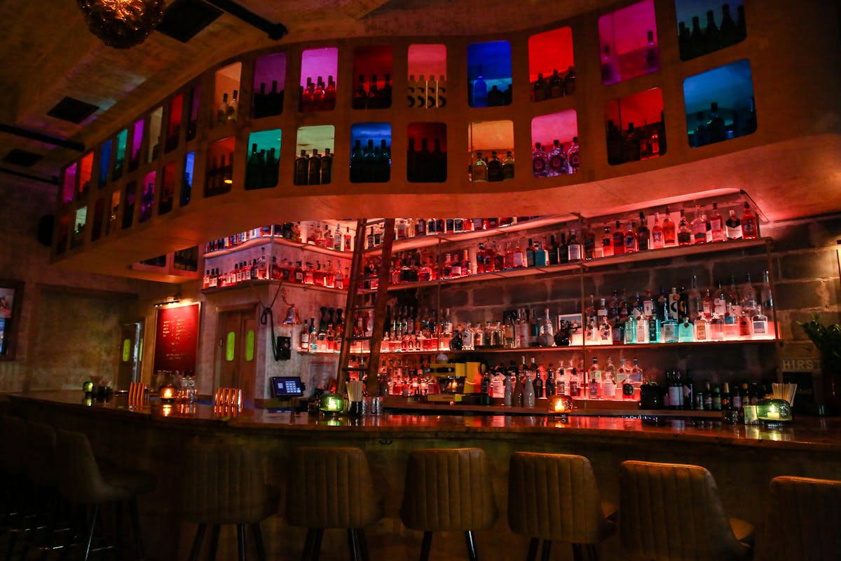 a cocktail bar with multi colored panels, lights, stools, and burl bar