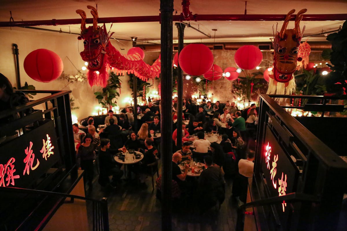 a dim lit dining room with a crowd of people having dinner with a red dragon and lantern decor