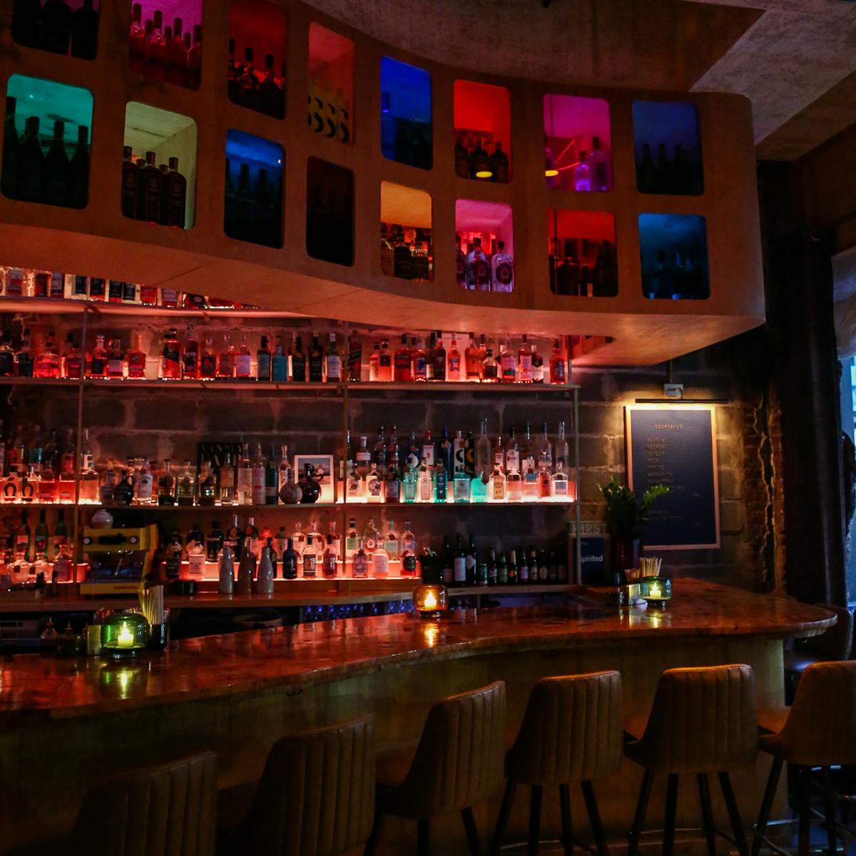 a cocktail bar with multi colored panels, lights, stools, and burl bar