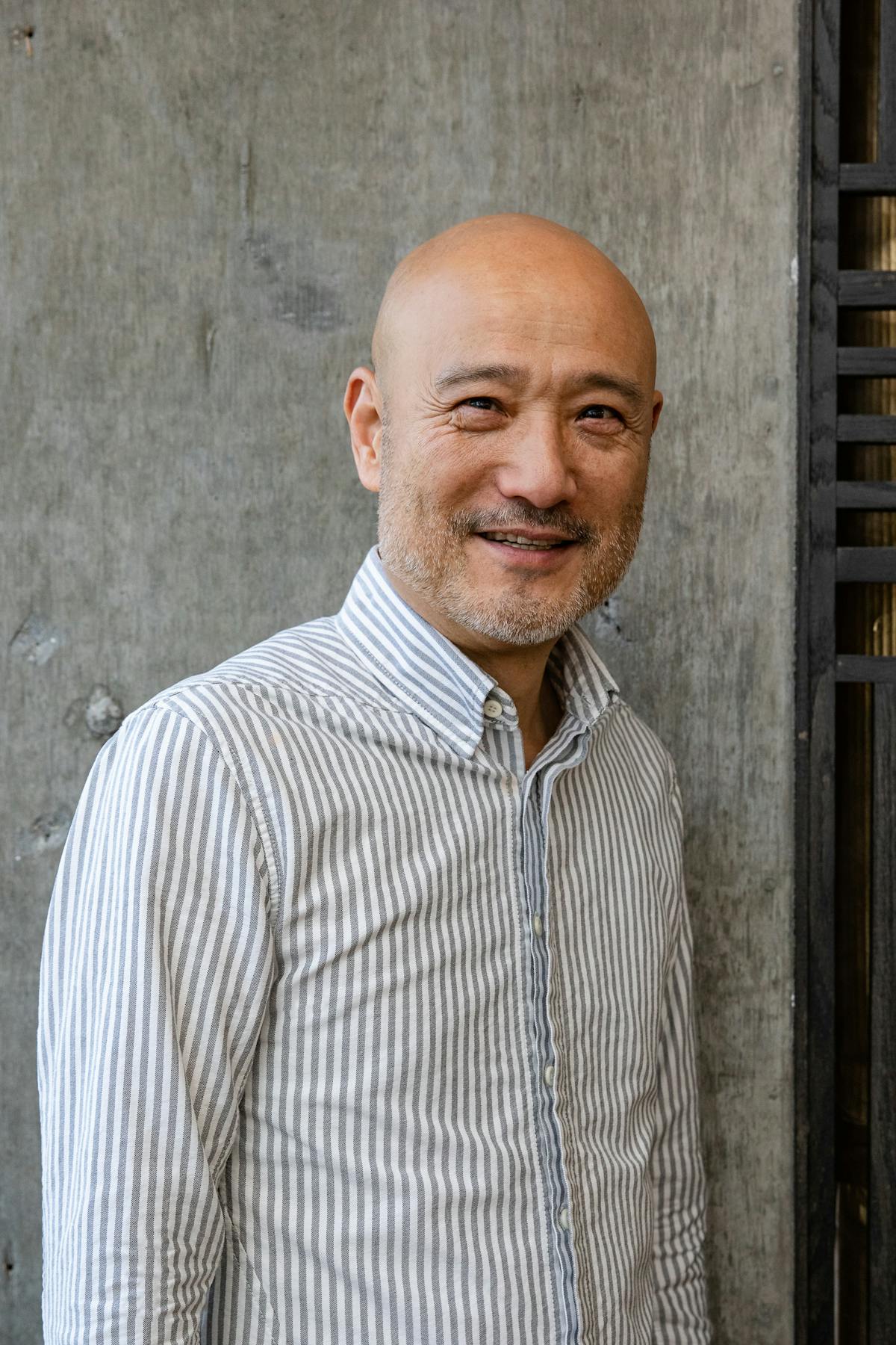 a bald man wearing a striped button down smiling