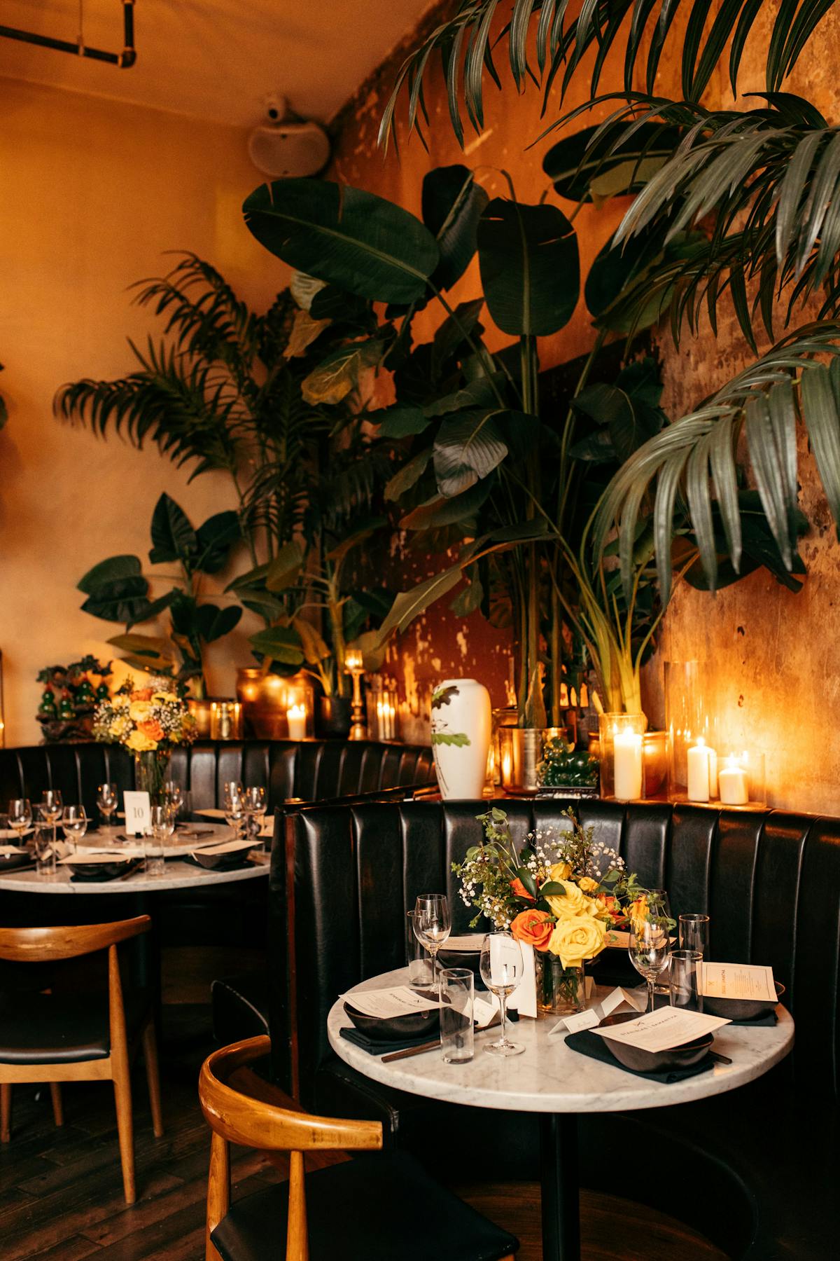 a dining room table with candles, plants, tables, and chairs