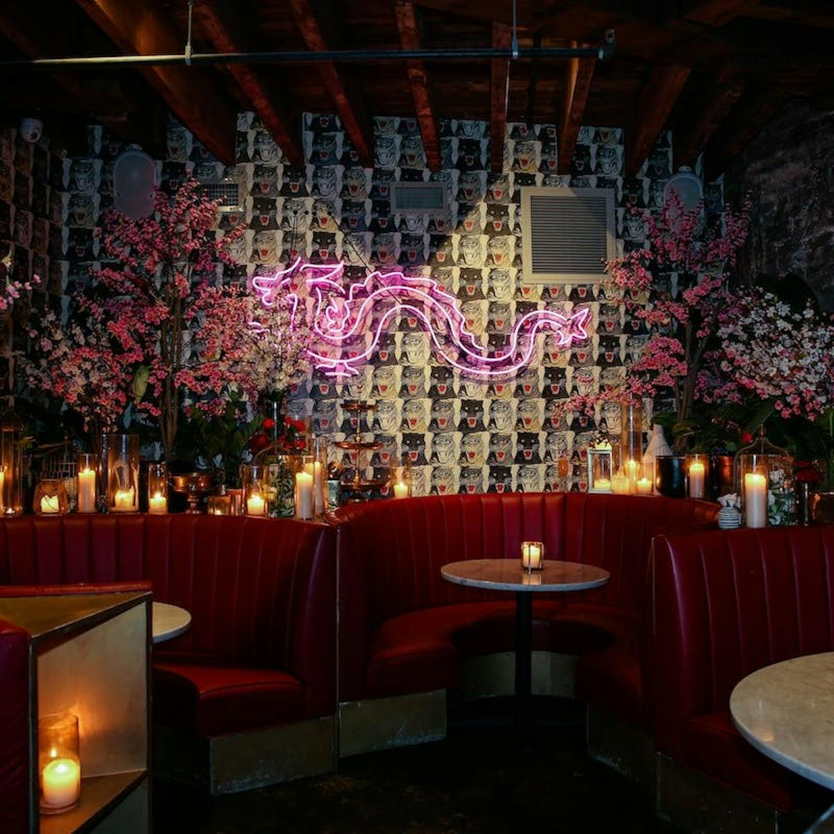 a cocktail bar with red booths, marble tables, candles, flowers, and a neon sign