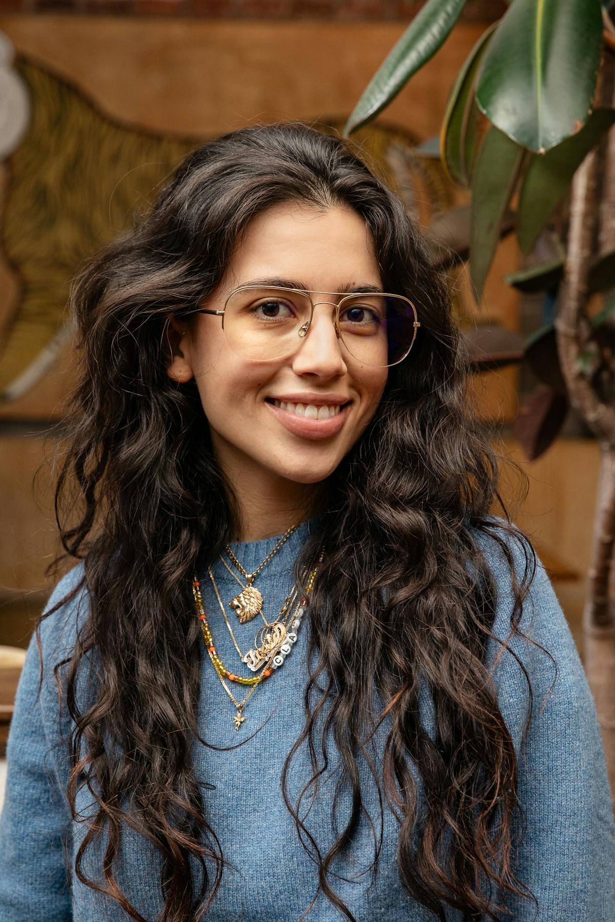a woman with long curly hair wearing glasses and a blue sweater smiling