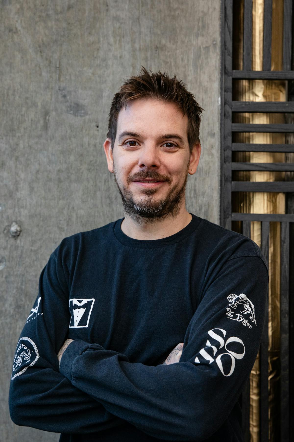 a man with short hair wearing a black long sleeve shirt smiling