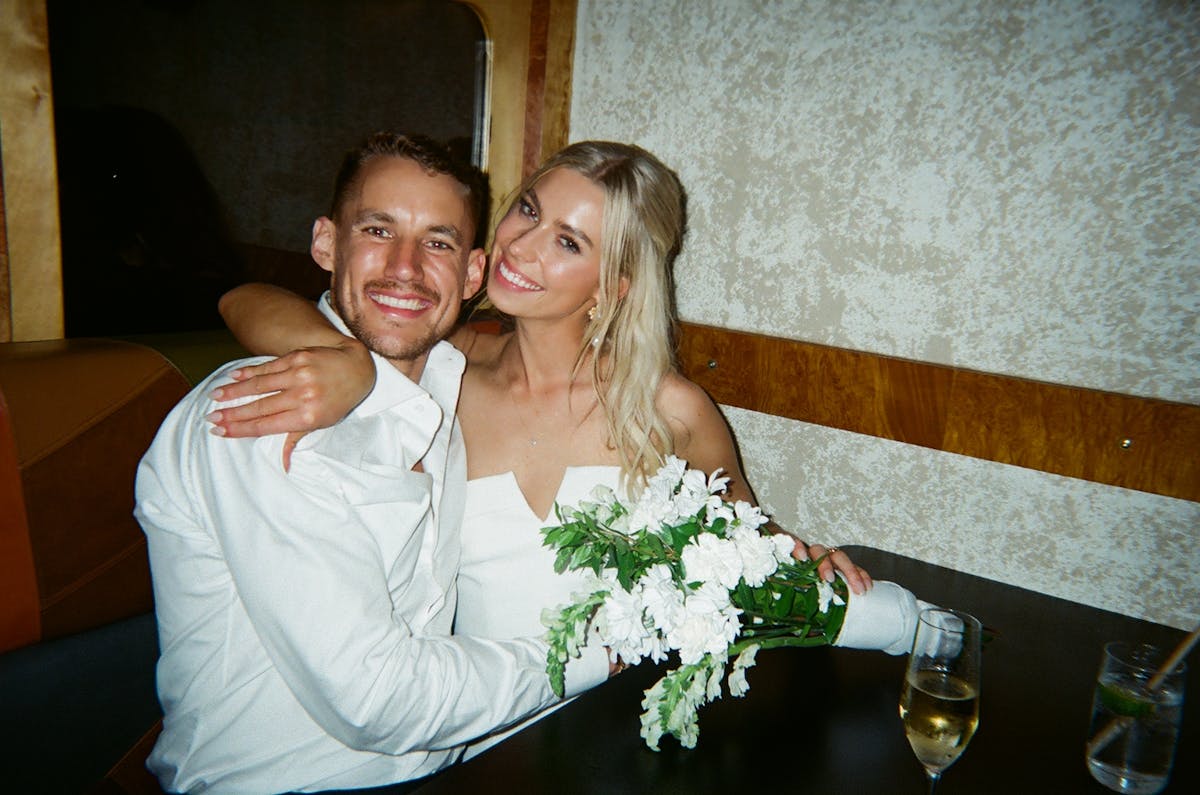 a bride and groom wearing white with flowers smiling