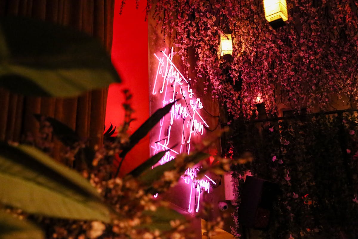 a close up of a pink neon sign with hanging lanterns and flowers
