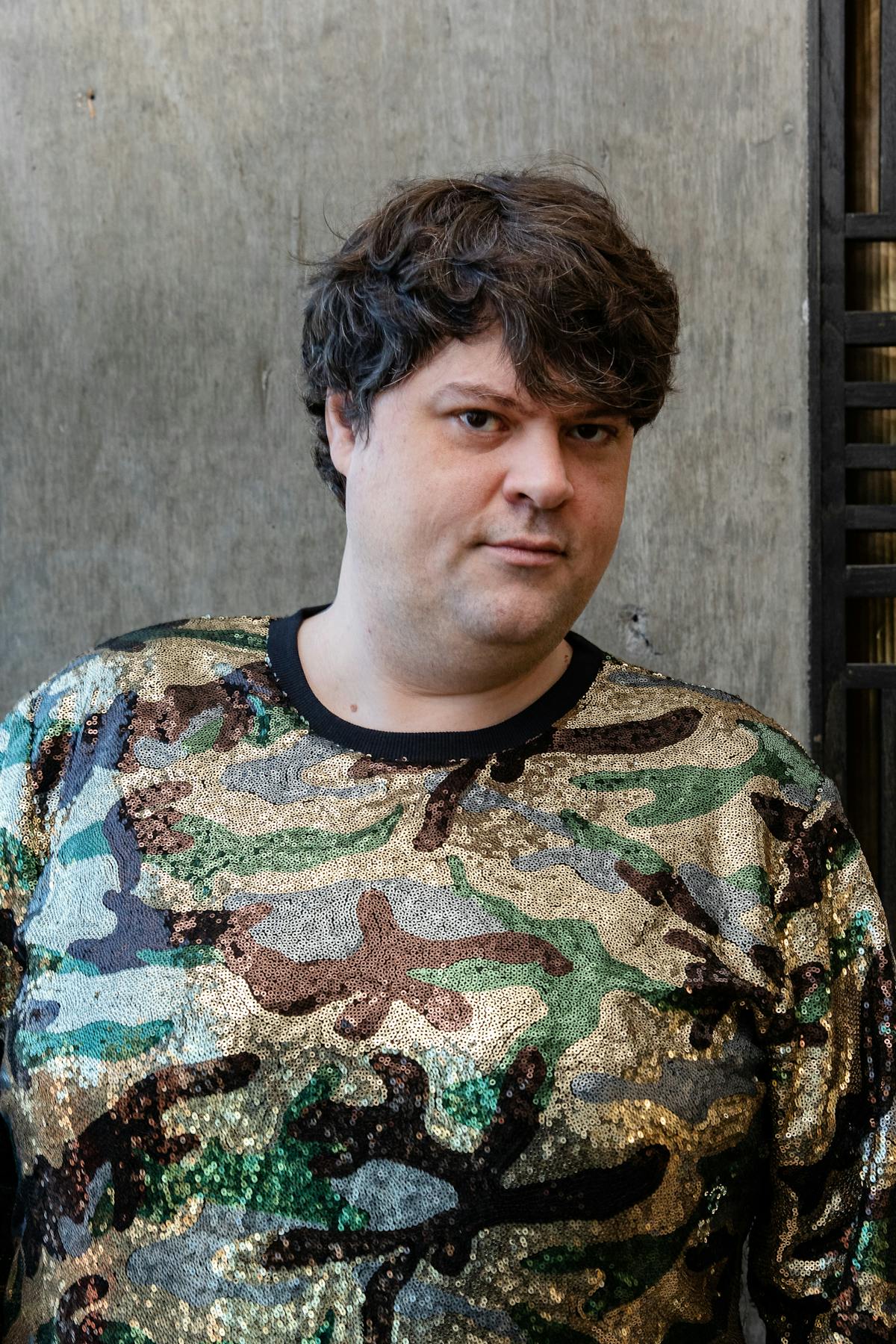 a man with short hair wearing sequin camo print smiling