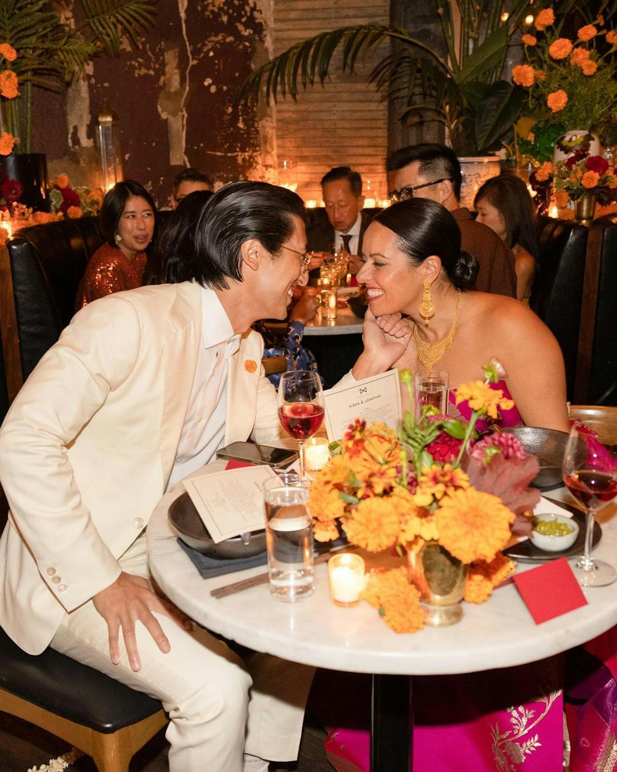 a bride and groom seated at their table smiling 