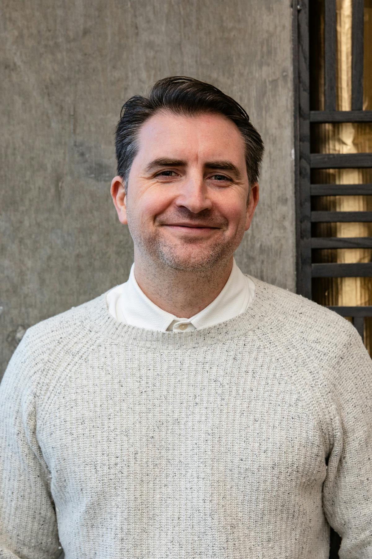 a man with short hair wearing an off-white sweater smiling