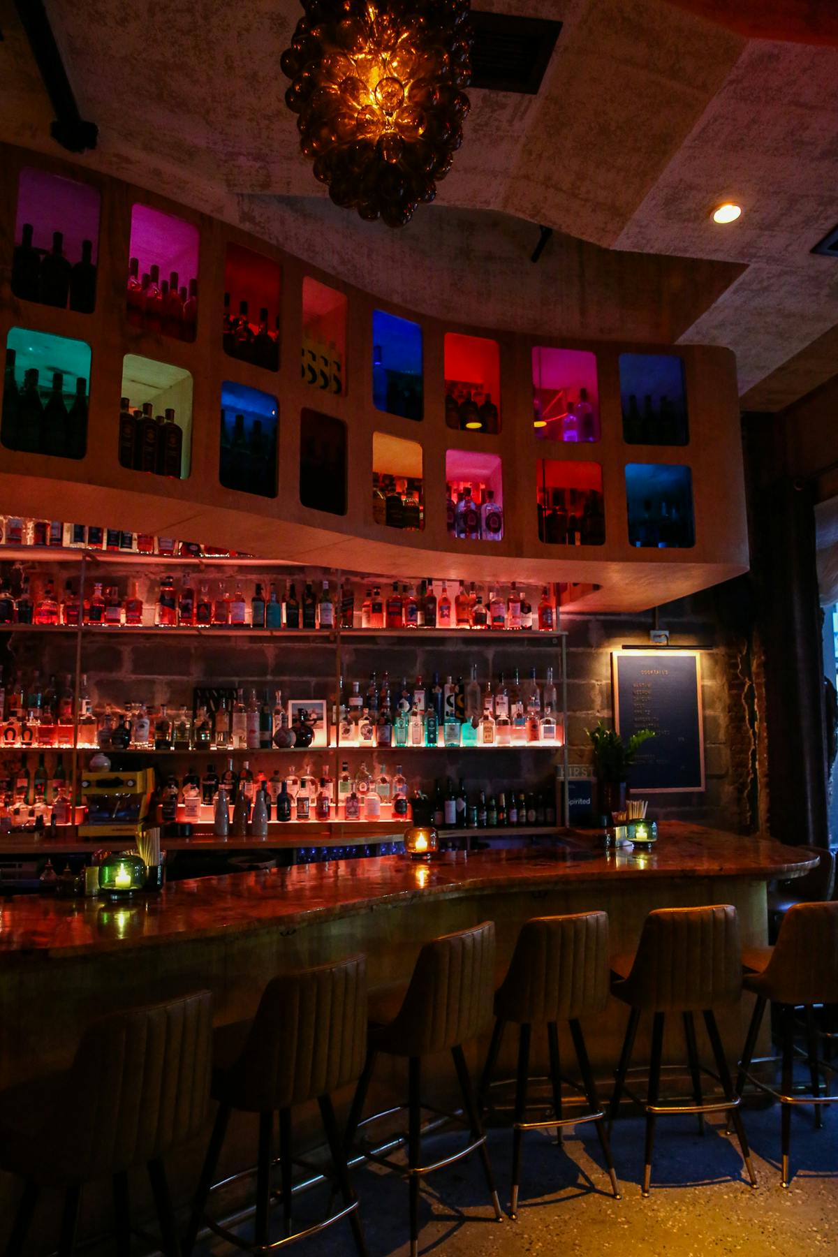 a cocktail bar with multi colored panels and lights with stools and a wooden bar