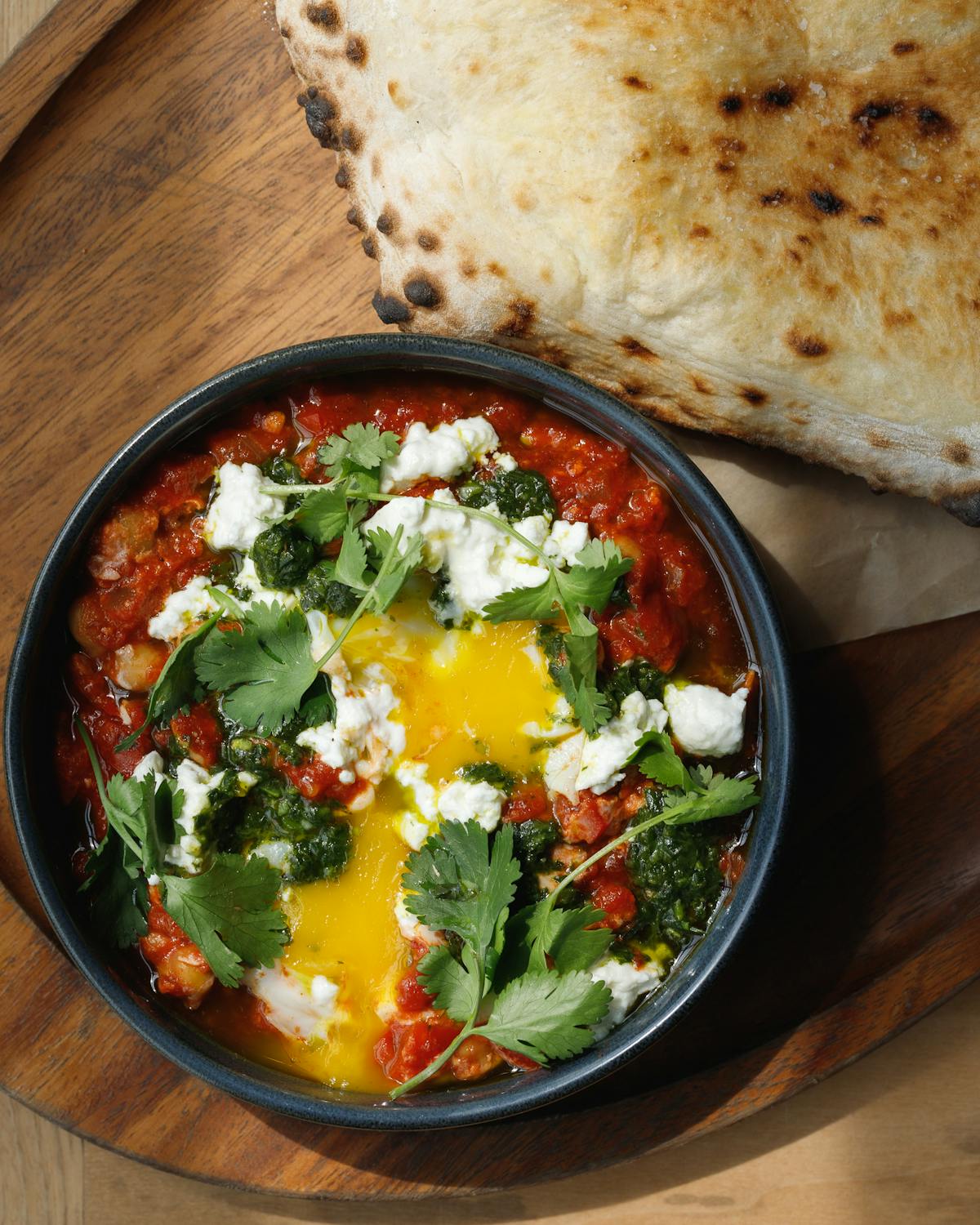 Shakshuka with tomato harissa sauce, chickpeas, feta, two eggs and hearth-baked pita