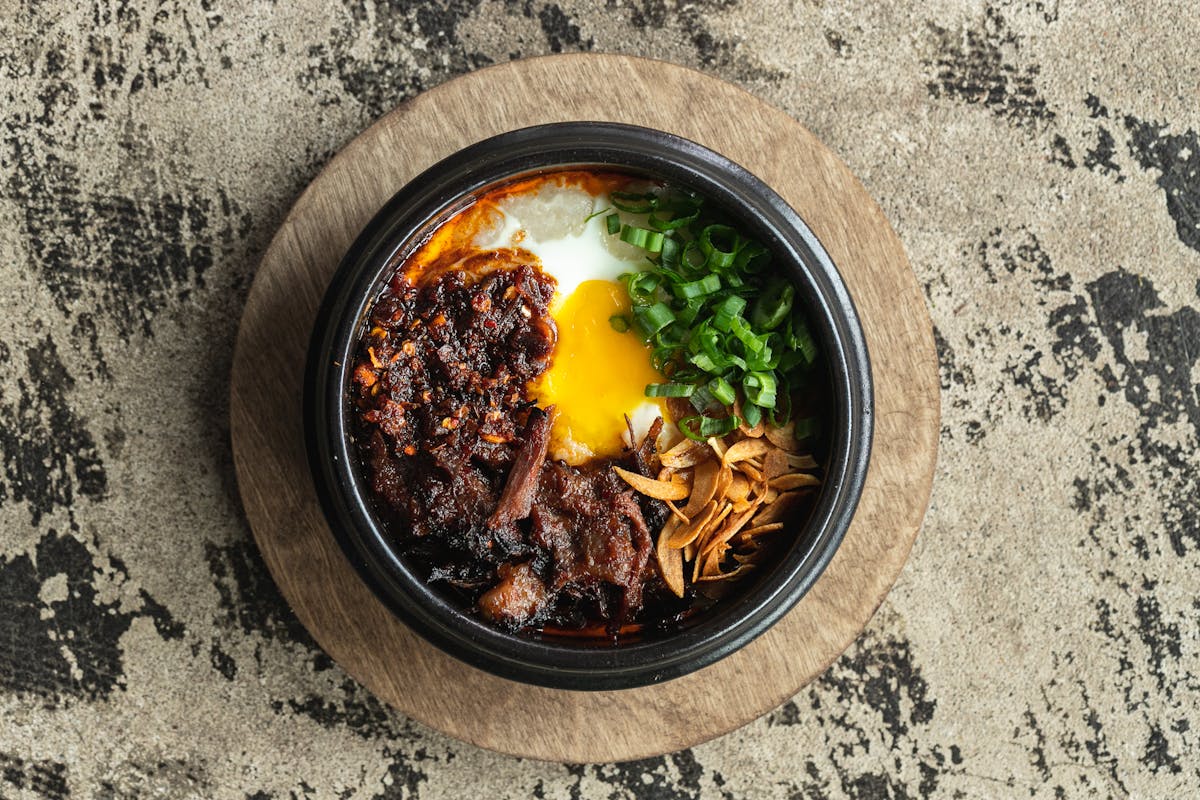 A bowl of Juk, rice congee with a poached egg, Korean short rib, crispy garlic, scallion and chile crisp
