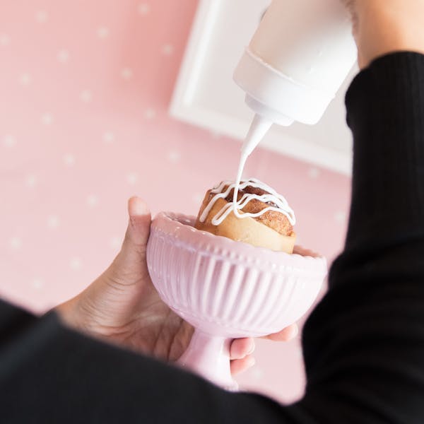 a person pouring sauces on a cupcake
