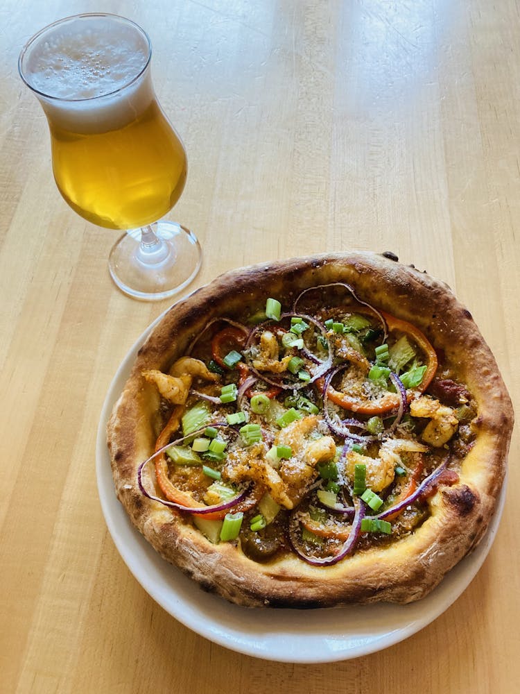 a special shrimp etouffee pizza on a table accompanied by a glass of beer