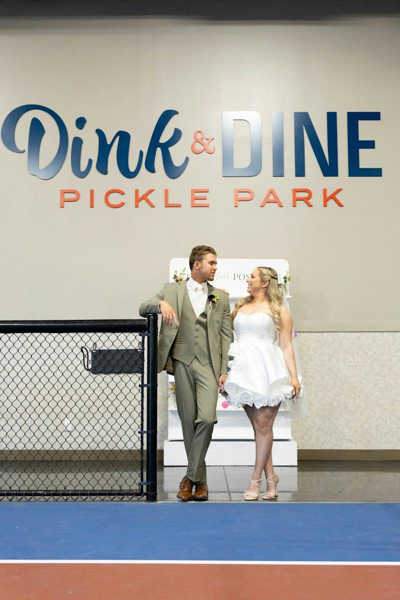 Bride and groom in front of the Dink & Dine Pickle Park sign