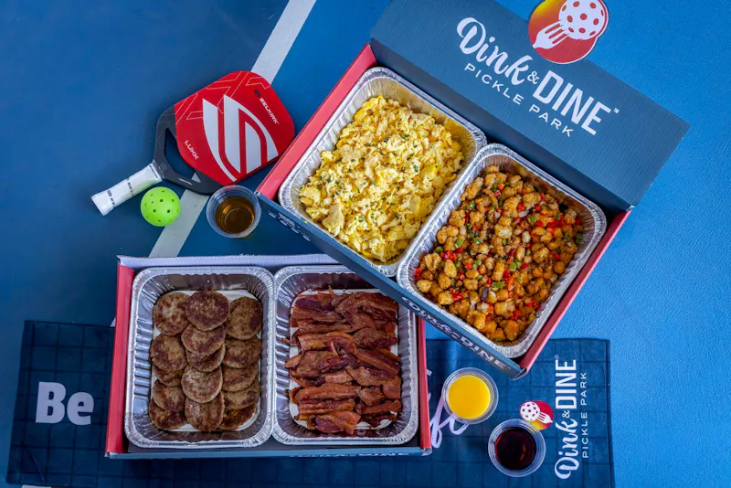 Breakfast catering trays of scrambled eggs, breakfast potatoes, sausage patties and bacon in Dink & Dine boxes at Dink & Dine Pickle Park