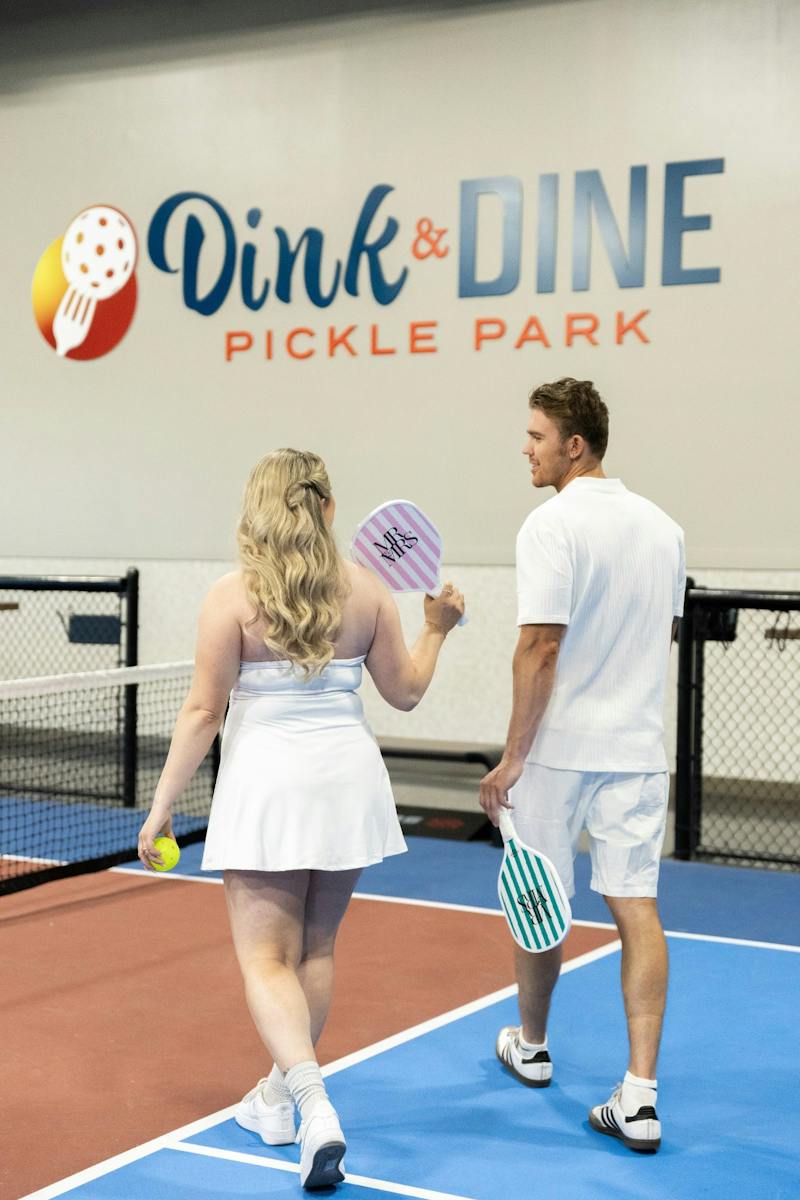 Bride and groom playing pickleball under the Dink & Dine Pickle Park sign