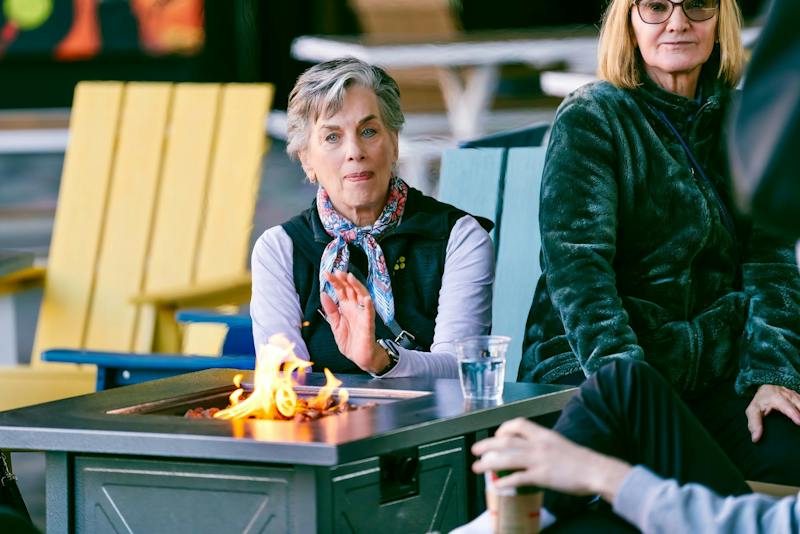 Guests relaxing around a fire pit in yellow Adirondack chairs at Dink & Dine Pickle Park