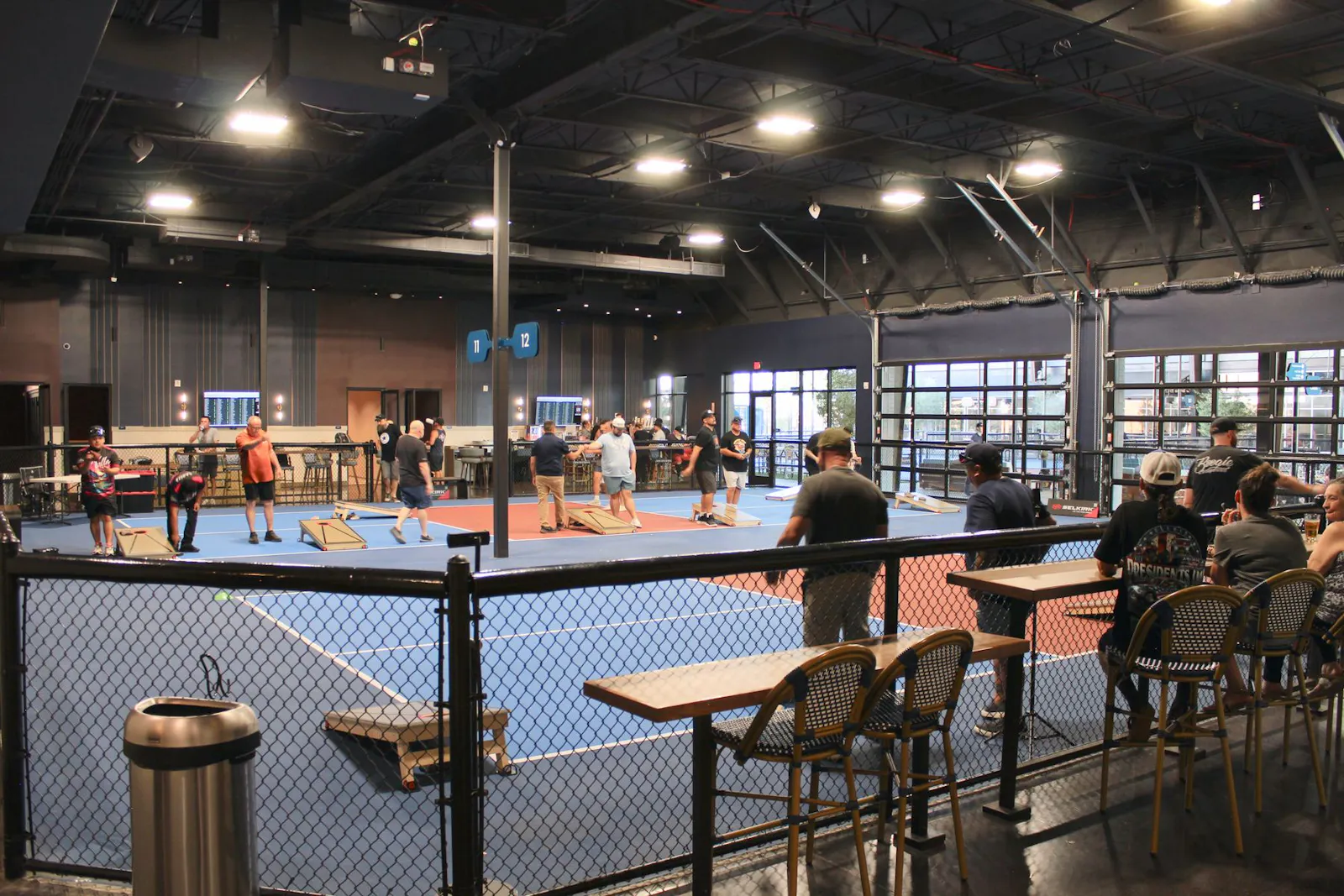 Indoor cornhole at Dink & Dine Pickle Park with bar seating along the rail