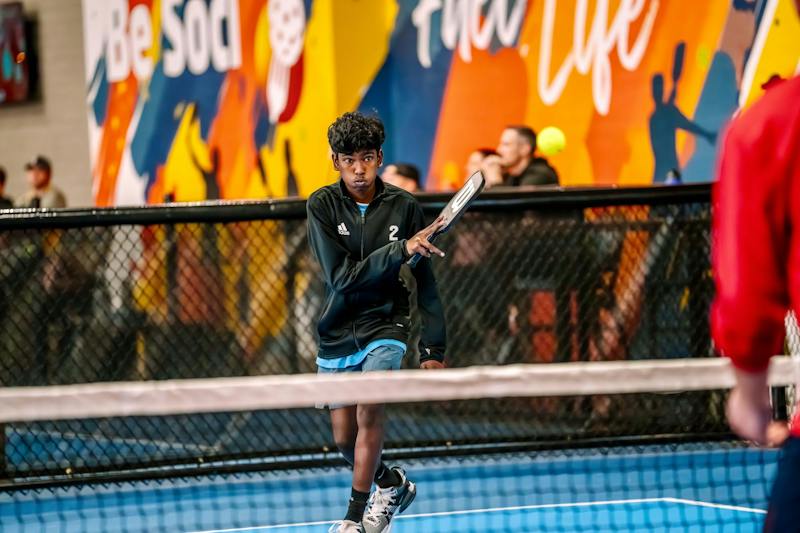 Player at the net in front of the Be Social Fuel Life mural at Dink & Dine Pickle Park