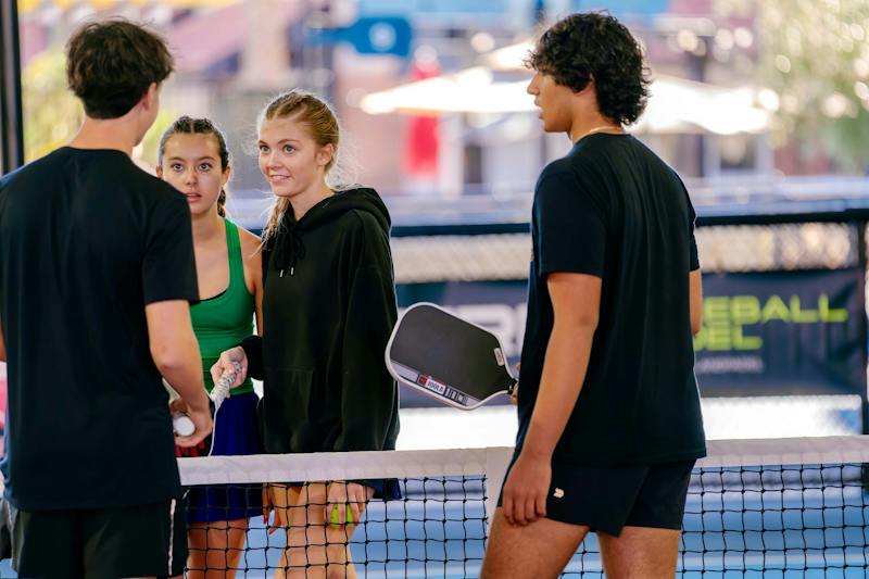 Friends chatting at the net on a pickleball court at Dink & Dine Pickle Park