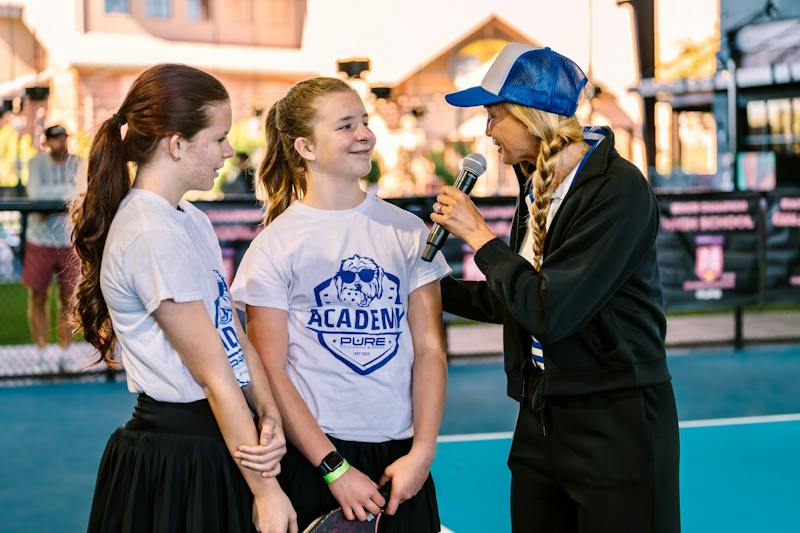 Two smiling players talking with an event host holding a microphone at Dink & Dine Pickle Park