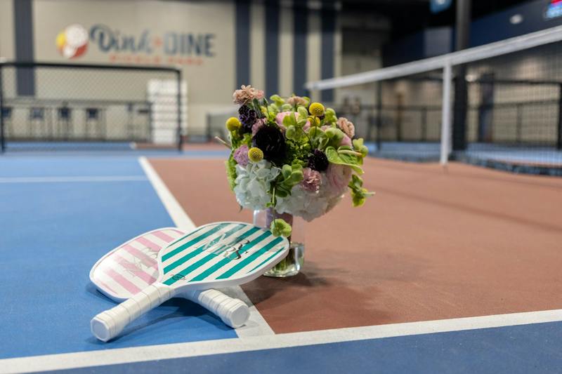 Mr. and Mrs. paddles and wedding flowers on a pickleball court at Dink & Dine Pickle Park