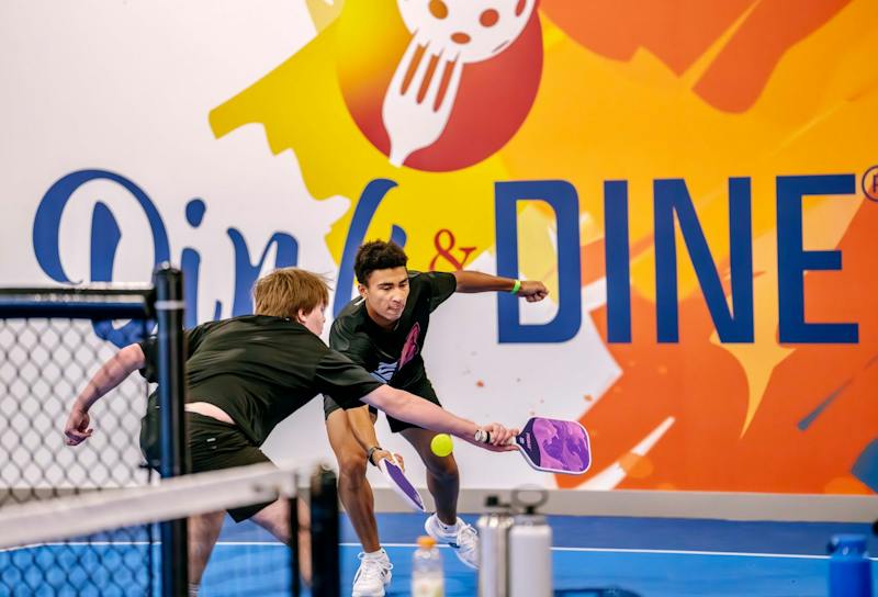 Player lunging for a shot in front of the big Dink and Dine mural at Dink & Dine Pickle Park