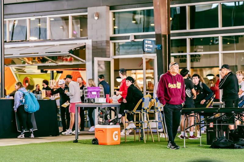 Crowd gathered around tables on the turf lawn at Dink & Dine Pickle Park