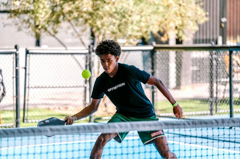 Player in the ready position at the net on an outdoor court at Dink & Dine Pickle Park