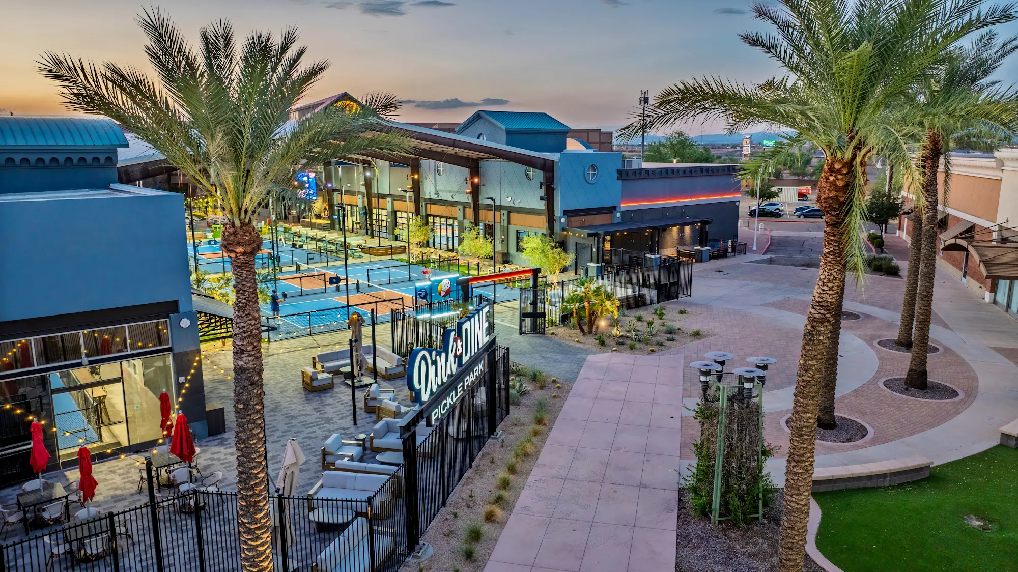 Aerial view of Dink & Dine Pickle Park at sunset with palm trees, outdoor pickleball courts and the main entrance