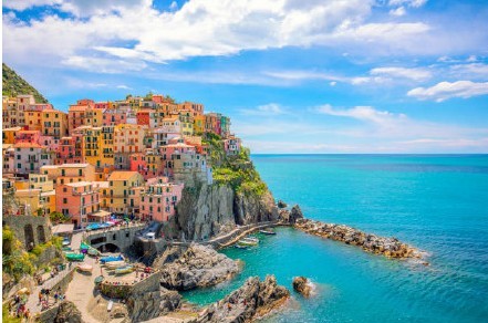 a colorful buildings on a cliff by the water with Cinque Terre in the background