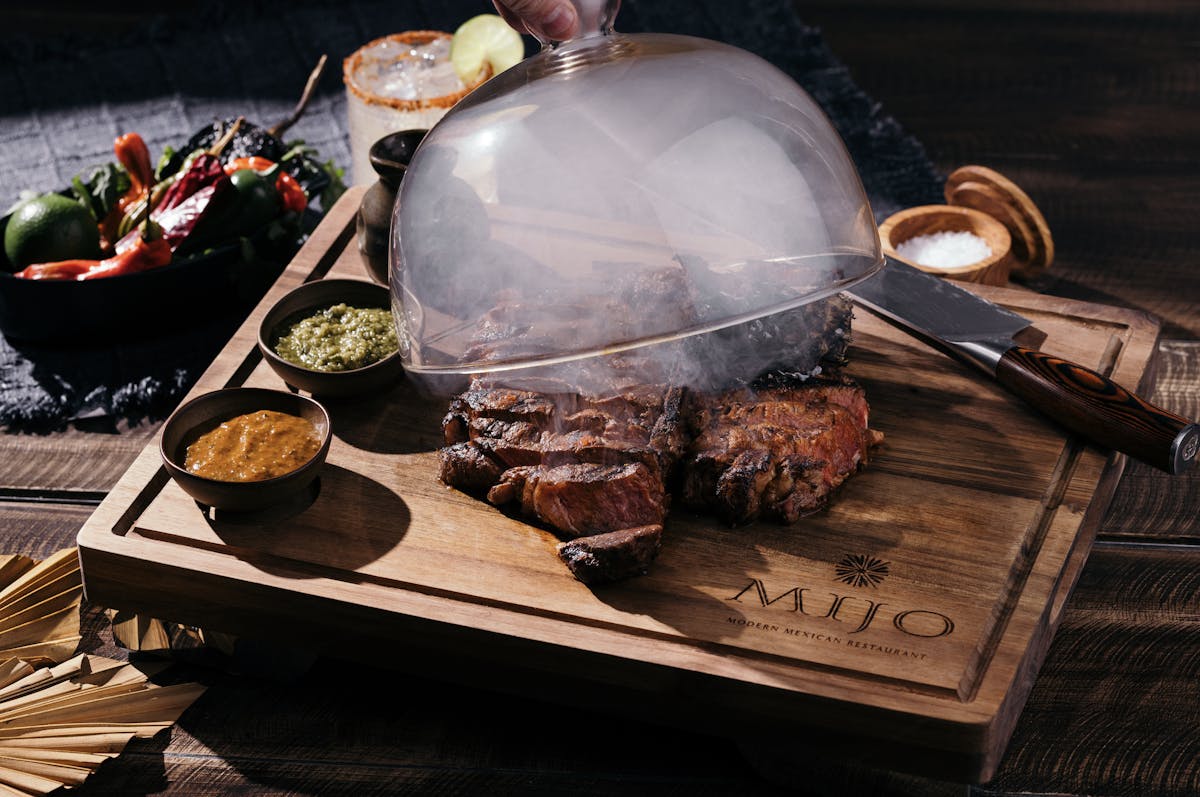 Food at Mijo Modern Mexican on a cutting board with sauces and smoke