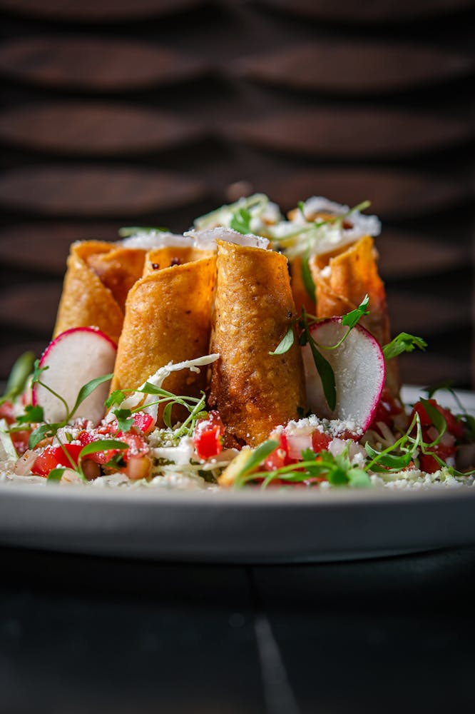 Crispy golden taquitos served upright with sliced radish, pico de gallo, cotija cheese, and fresh microgreens at Mijo Modern Mexican.