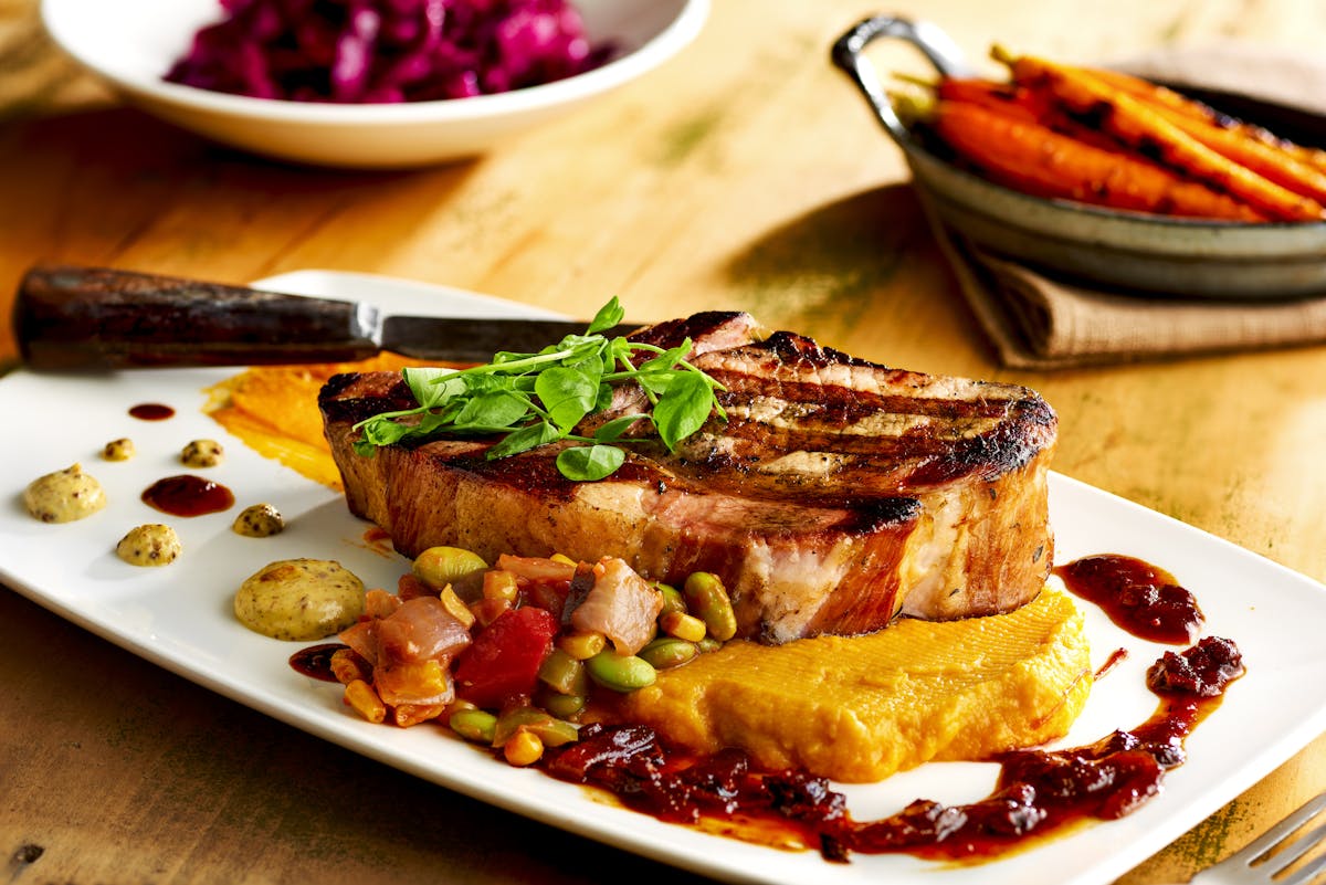 close up of a pork chop on a dish with various sides