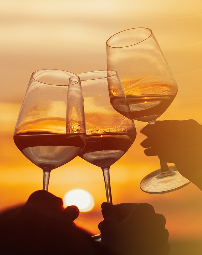 Three people hold up wine glasses against a golden sunset
